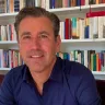 A man in a blue shirt sitting in front of a bookcase