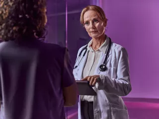 Healthcare professional holding a tablet listens intently to her colleague
